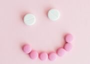 Smiley face made from pink and white tablets on a pastel pink background.